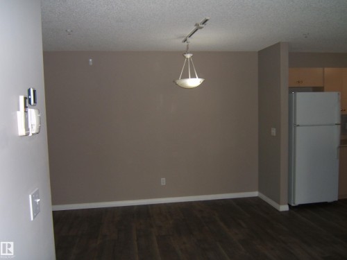Spacious interior featuring dark wood-finish flooring, a contemporary pendant light fixture, and track lighting - 105 11214 80 Street, Edmonton, AB - Indoor
