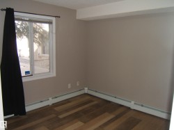 Wood-finish flooring throughout, featuring a window with white trim, baseboard heating, and neutral wall tones - 