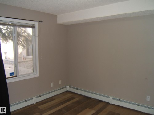 Room featuring wood-finish flooring, a window with white trim, and baseboard heating - 105 11214 80 Street, Edmonton, AB - Indoor Photo Showing Other Room