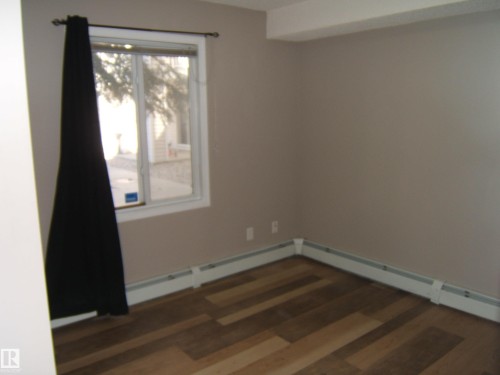 Room featuring wood-finish flooring, neutral wall paint, and a white-framed window - 105 11214 80 Street, Edmonton, AB - Indoor Photo Showing Other Room