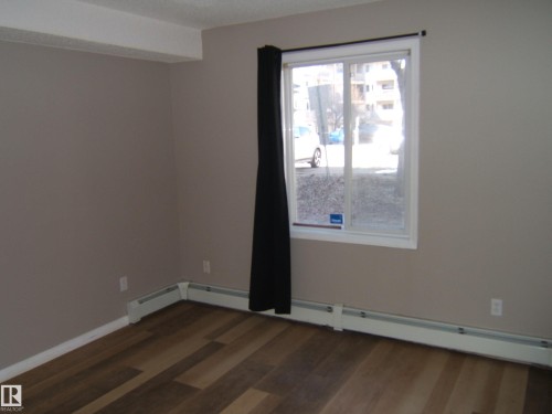 Neutral tone walls with wood-finish flooring, white baseboards, and a window featuring a white frame - 105 11214 80 Street, Edmonton, AB - Indoor Photo Showing Other Room