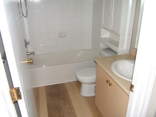 Bathroom featuring a white tub, shower with white tiled surround, and wood-finish flooring - 105 11214 80 Street, Edmonton, AB - Indoor Photo Showing Bathroom