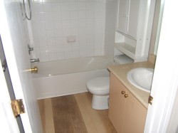 Bathroom featuring a white tub, shower with white tiled surround, and wood-finish flooring - 