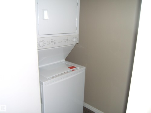 Stackable white laundry appliances with a neutral wall color and white baseboard trim - 105 11214 80 Street, Edmonton, AB - Indoor Photo Showing Laundry Room