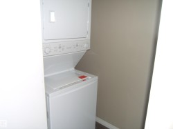 Stackable white laundry appliances with a neutral wall color and white baseboard trim - 