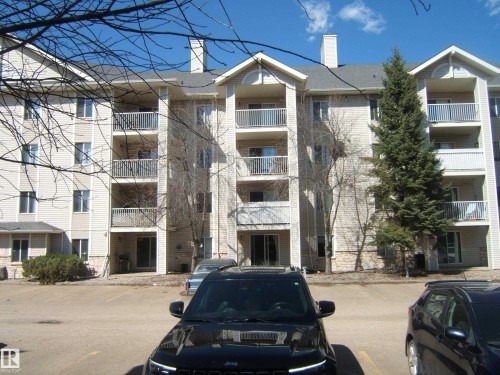 Multi-story residential building featuring light-toned horizontal siding, multiple private balconies with white railings, and a lower level with stone facade detailing - 105 11214 80 Street, Edmonton, AB - Outdoor With Facade