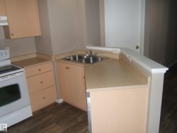 Kitchen featuring a double basin stainless steel sink, light-toned countertops, wood-finish flooring, and light peach cabinetry with brass hardware - 