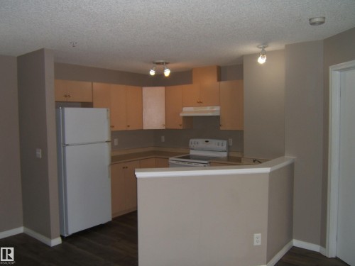 Kitchen featuring wood-finish flooring, light wood cabinetry, white appliances, and a breakfast bar peninsula - 105 11214 80 Street, Edmonton, AB - Indoor Photo Showing Kitchen
