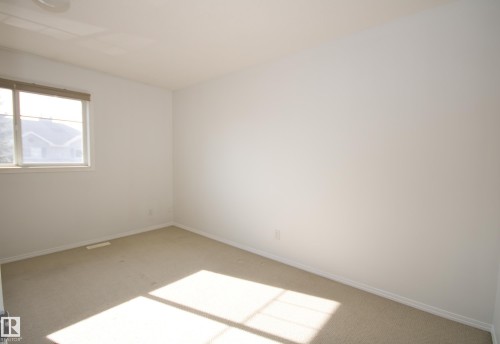 Spacious room featuring neutral carpeting, white wall finishes, and a casement window with a neutral-toned shade - 11 230 Edwards Drive, Edmonton, AB - Indoor Photo Showing Other Room