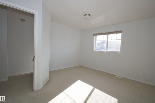 Bright interior room featuring a window with integrated blinds, neutral carpeting, and a flush-mount ceiling light fixture - 11 230 Edwards Drive, Edmonton, AB - Indoor Photo Showing Other Room