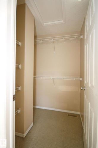 Walk-in closet featuring carpet flooring, neutral paint, white wire shelving, and an attic access panel - 11 230 Edwards Drive, Edmonton, AB - Indoor With Storage