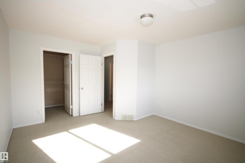 Neutral tone wall paint, light-toned carpet flooring, a flush mount ceiling light fixture, two paneled interior doors, and a built-in wire shelf closet system - 11 230 Edwards Drive, Edmonton, AB - Indoor Photo Showing Other Room