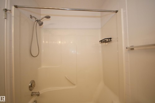 Fiberglass shower and tub combination featuring a chrome dual showerhead, built-in shelving, and a chrome towel bar - 11 230 Edwards Drive, Edmonton, AB - Indoor Photo Showing Bathroom