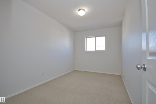 Carpeted interior room featuring a window, ceiling-mounted light fixture, white walls, and baseboards - 11 230 Edwards Drive, Edmonton, AB - Indoor Photo Showing Other Room