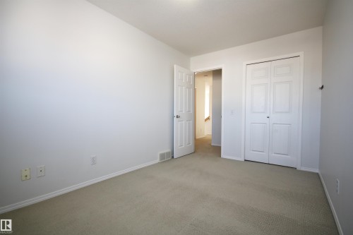 Neutral-toned carpeting and white walls in this room with a white bi-fold closet door - 11 230 Edwards Drive, Edmonton, AB - Indoor Photo Showing Other Room