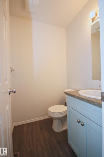 Powder room featuring wood-finish flooring, a light blue vanity with cabinet storage, a white porcelain sink, and a speckled countertop - 11 230 Edwards Drive, Edmonton, AB - Indoor Photo Showing Bathroom