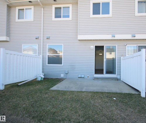 Rear exterior featuring light-toned horizontal siding, a concrete patio, and a sliding glass door - 11 230 Edwards Drive, Edmonton, AB - Outdoor With Exterior