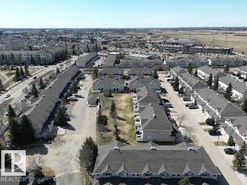 Residential development featuring rows of multi-unit buildings, mature evergreen trees, paved parking areas, and green spaces - 11 230 Edwards Drive, Edmonton, AB - Outdoor With View