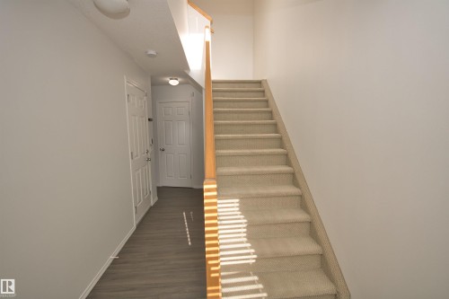 Carpeted staircase with light wood handrail, white painted walls, and wood-finish flooring in the hallway - 11 230 Edwards Drive, Edmonton, AB - Indoor Photo Showing Other Room