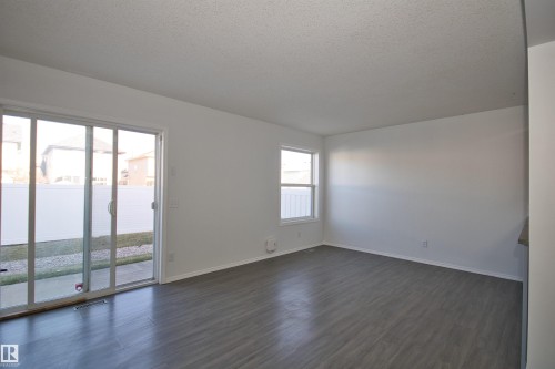 Spacious room featuring wood-finish flooring, a large sliding glass door, and an additional window - 11 230 Edwards Drive, Edmonton, AB - Indoor Photo Showing Other Room