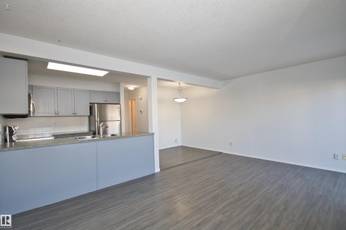 Open-concept living area featuring wood-finish flooring, a kitchen with light gray cabinetry, stainless steel appliances, and a breakfast bar - 11 230 Edwards Drive, Edmonton, AB - Indoor Photo Showing Kitchen With Double Sink