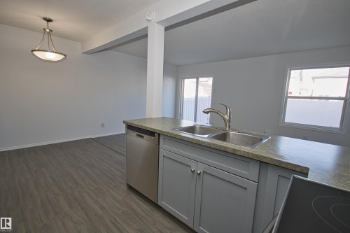 Kitchen island featuring a double basin stainless steel sink, brushed nickel faucet, and a light-toned countertop - 11 230 Edwards Drive, Edmonton, AB - Indoor Photo Showing Kitchen With Double Sink