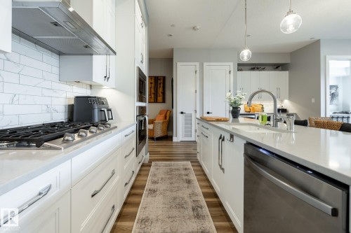 Contemporary kitchen featuring white cabinetry, light countertops, wood-finish flooring, a gas range with a stainless steel hood, and integrated stainless steel appliances - 108 7463 May Common, Edmonton, AB - Indoor Photo Showing Kitchen With Upgraded Kitchen
