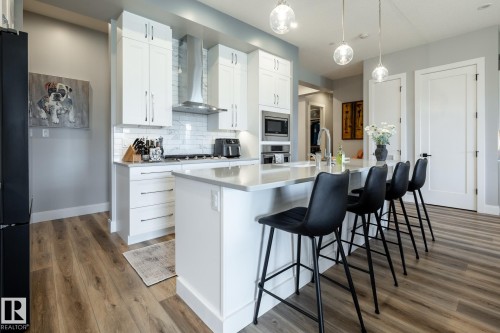 Modern kitchen featuring a central island with seating, pendant lighting, and stainless steel appliances - 108 7463 May Common, Edmonton, AB - Indoor Photo Showing Kitchen With Upgraded Kitchen