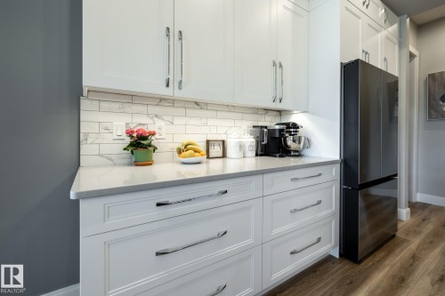 White shaker-style cabinetry with chrome hardware, light-toned countertop, subway tile backsplash, and dark-finish refrigerator - 108 7463 May Common, Edmonton, AB - Indoor Photo Showing Kitchen