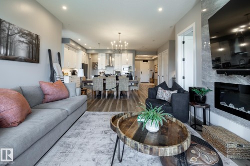 Open-concept living space with wood-finish flooring, recessed lighting, and a stone-clad fireplace - 108 7463 May Common, Edmonton, AB - Indoor Photo Showing Living Room With Fireplace