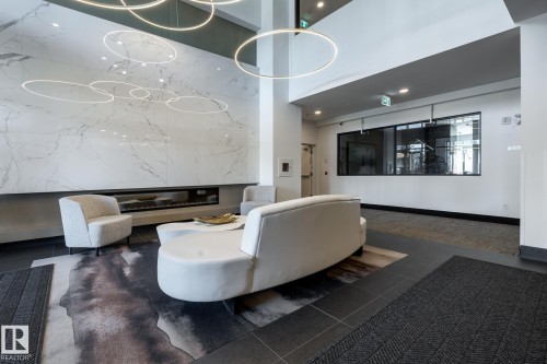 Lobby area featuring a full-height marble-look wall with an integrated linear fireplace, illuminated by contemporary circular pendant lighting - 108 7463 May Common, Edmonton, AB - Indoor Photo Showing Other Room