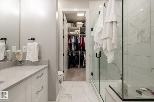 Bathroom featuring a glass-enclosed shower with white marble-look tile, a single vanity with a light gray countertop, white cabinetry with silver-toned hardware, and a walk-in closet with built-in shelving - 108 7463 May Common, Edmonton, AB - Indoor Photo Showing Bathroom