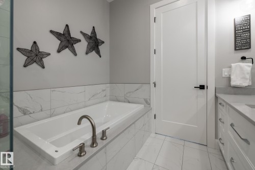 Built-in bathtub with brushed nickel fixtures, surrounded by large format tile with subtle veining - 108 7463 May Common, Edmonton, AB - Indoor Photo Showing Bathroom
