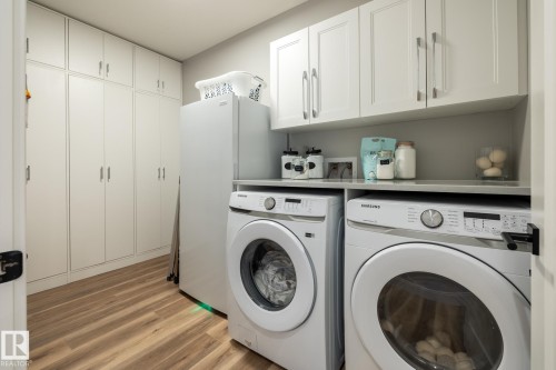 Dedicated laundry area featuring wood-finish flooring, extensive white built-in cabinetry, upper wall cabinets, and a solid-surface countertop - 108 7463 May Common, Edmonton, AB - Indoor Photo Showing Laundry Room