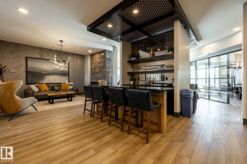 Open-concept room featuring wood-finish flooring, a built-in bar with dark countertops and open shelving, and a modern chandelier - 108 7463 May Common, Edmonton, AB - Indoor