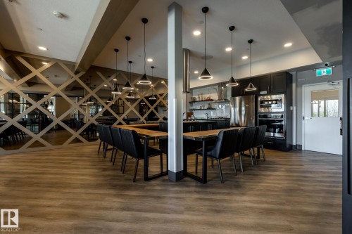 Open-concept common area featuring wood-finish flooring, a contemporary kitchen with stainless steel appliances, dark cabinetry, and an integrated dining table - 108 7463 May Common, Edmonton, AB - Indoor Photo Showing Dining Room