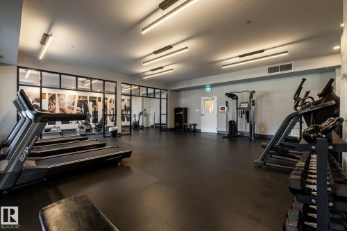 Fitness center with rubber flooring, linear overhead lighting, and frosted glass partition walls - 108 7463 May Common, Edmonton, AB - Indoor Photo Showing Gym Room