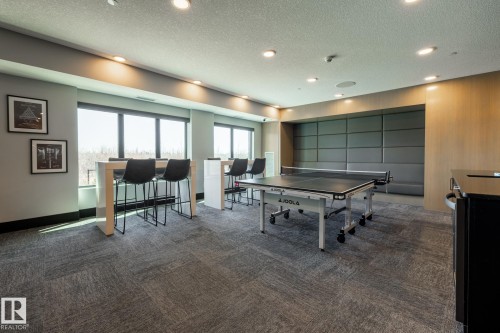 Spacious room featuring textured gray carpet, recessed lighting, and expansive windows - 108 7463 May Common, Edmonton, AB - Indoor Photo Showing Other Room
