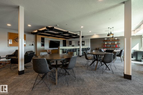 Spacious recreation room featuring carpet flooring, recessed lighting, a modern bar area with bar stool seating, and multiple dining and lounge areas - 108 7463 May Common, Edmonton, AB - Indoor