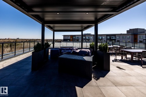 Rooftop patio with a black metal pergola featuring recessed lighting, a glass-paneled railing, and square-format tile flooring - 108 7463 May Common, Edmonton, AB - Outdoor With Exterior