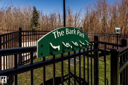 Dedicated pet park with a robust metal fence, a green park sign, and a paved entry path, surrounded by natural landscaping - 108 7463 May Common, Edmonton, AB - Outdoor