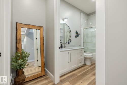 Bathroom featuring wood-finish flooring, a white vanity with a light-colored countertop, and a circular mirror - 108 7463 May Common, Edmonton, AB - Indoor Photo Showing Bathroom