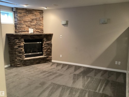 Stone-clad fireplace with a built-in electric insert, complemented by track lighting, wall sconces, and neutral wall tones - 54 Leonard Drive, St. Albert, AB - Indoor With Fireplace