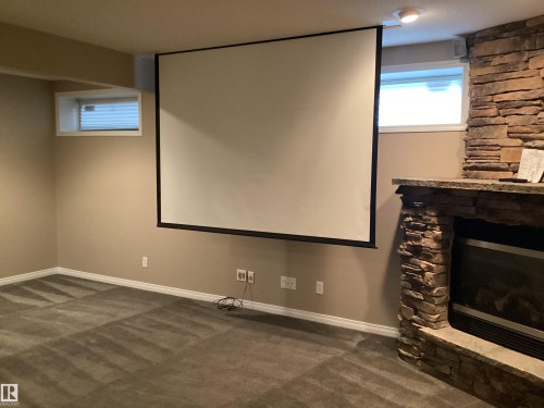 Entertainment area featuring a projector screen, stone-clad fireplace with mantel, recessed lighting, and carpet flooring - 54 Leonard Drive, St. Albert, AB - Indoor Photo Showing Other Room With Fireplace