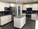 Modern kitchen featuring white shaker-style cabinetry, a central island, stainless steel appliances, dark stone-look countertops, and a dark tile backsplash - 54 Leonard Drive, St. Albert, AB  - Indoor Photo Showing Kitchen 