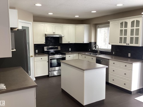 Kitchen featuring white cabinetry, dark countertops, and a dark tile backsplash - 54 Leonard Drive, St. Albert, AB - Indoor Photo Showing Kitchen With Double Sink