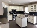 Kitchen featuring white cabinetry, dark countertops, and a dark tile backsplash - 54 Leonard Drive, St. Albert, AB  - Indoor Photo Showing Kitchen With Double Sink 