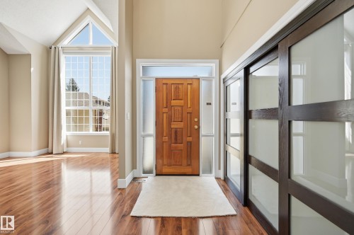 Entryway featuring a paneled wood-finish door with frosted sidelights and transom window, wood-finish flooring, vaulted ceilings, and a tall picture window with grid detailing - 394 Walker Road, Edmonton, AB - Indoor Photo Showing Other Room