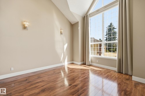 Vaulted ceiling living space featuring a large picture window with grid detailing, wood-finish flooring, two wall sconces, and neutral wall paint - 394 Walker Road, Edmonton, AB - Indoor Photo Showing Other Room
