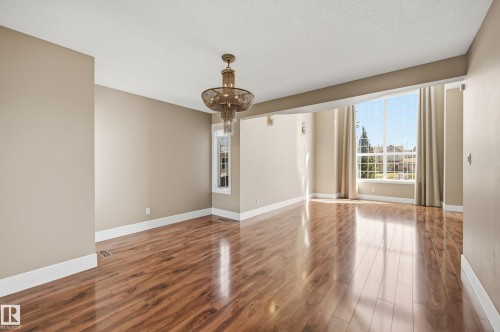 Spacious room featuring wood-finish flooring, a decorative chandelier, and a large window with white trim - 394 Walker Road, Edmonton, AB - Indoor Photo Showing Other Room